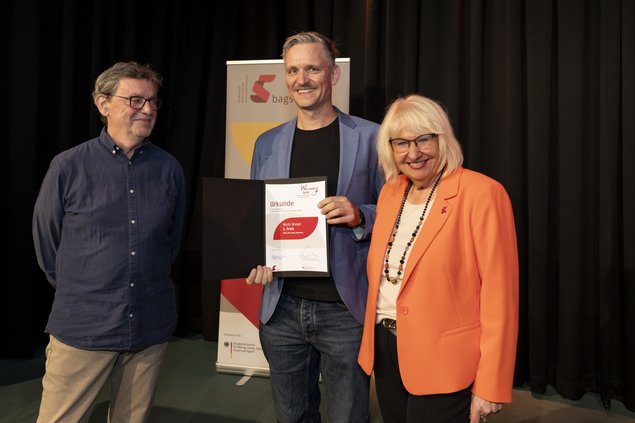 Zwei Männer, eine Frau. Der Mann in der Mitte hält eine Urkunde in der Hand. Klick öffnet eine vergrößerte Ansicht.