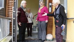 Drei alte Frauen stehen vor dem Eingang einer Haustür. Eine im Haus. Sie unterhalten sich lachend.