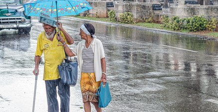 Ein altes Paar geht während eines Regenschauers über eine Straße. Sie hält ihm den Schirm. 