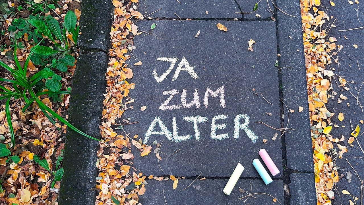 Auf einem Bürgersteig steht mit bunter Kreide "JA zum Alter" geschrieben.