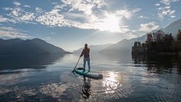 Eine Frau von hinten. Sie macht gerade Standup-Paddling auch einem See, der von Bergen umgeben ist.