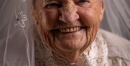 Seniorin mit einem Brautschleier, die von Herzen lächelt.