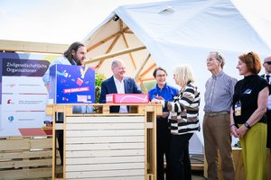 Drei Männer und drei Frauen stehen in einem Halbkreis um einen Messestand.