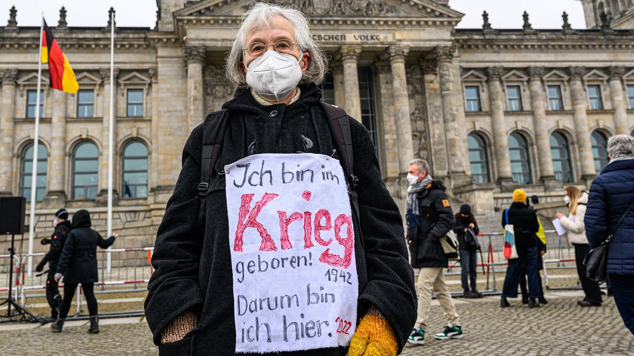 Eine alte Frau steht vor dem Bundestag mit einem Schild vor ihrem Bauch auf dem steht: Ich bin im Krieg geboren! 1942 - Darum bin ich hier. 2022