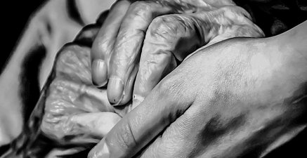 Die gefalteten Hände einer 90-jährigen Dame werden von jungen Händen berührt.