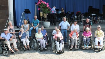 Gruppe älterer Menschen stehen vor einer Bühne
