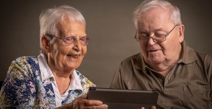 Älteres Ehepaar schaut lächelnd auf ein Tablet und lächelt.