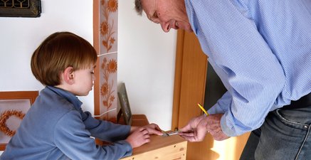 Älterer Mann zimmert eine kleine Kiste aus Holz. Sein Enkel geht ihm zur Hand.