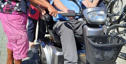 Älterer Herr sitzt im Elektroroller, umringt von drei gleichaltrigen Frauen