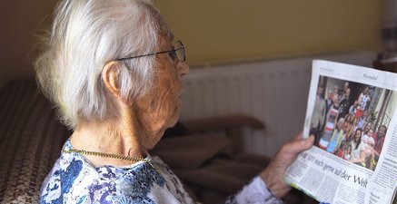 Alte Frau liest Zeitungsartikel über die Feier zu ihrem 101. Geburtstag