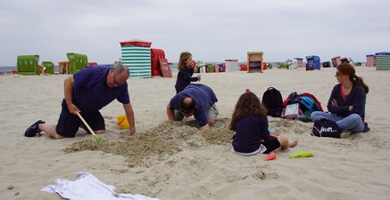 Drei Generationen bauen gemeinsam am Strand eine Sandburg.