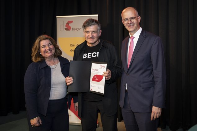 Zwei Männer, eine Frau. Der Mann, der in der Mitte steht, hält eine Urkunde in der Hand. Klick öffnet eine vergrößerte Ansicht.