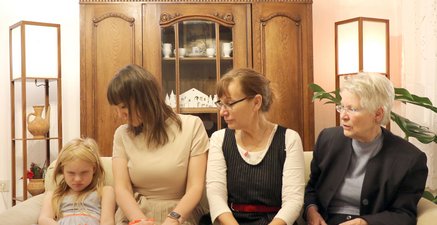 Vier weibliche Personen vier unterschiedlicher Generationen sitzen auf einem Sofa. Das kleine Mädchen schmollt.