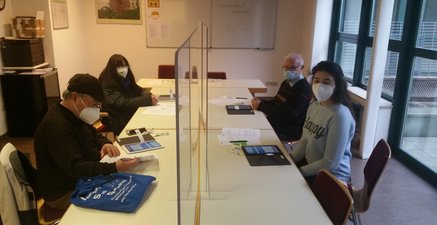 Es sind 4 Menschen, 3 Ältere und 1 Junge, die sich als Trainer auf eine Tabletschulung für Seniorinnen vorbereiten
