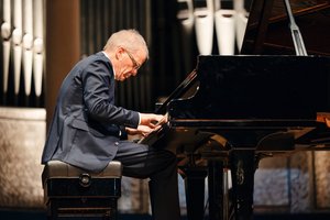 Auf der Bühne: Ein älterer Mann im dunklen Anzug, Professor Andreas Kruse,  sitzt an einem Flügel und spielt.