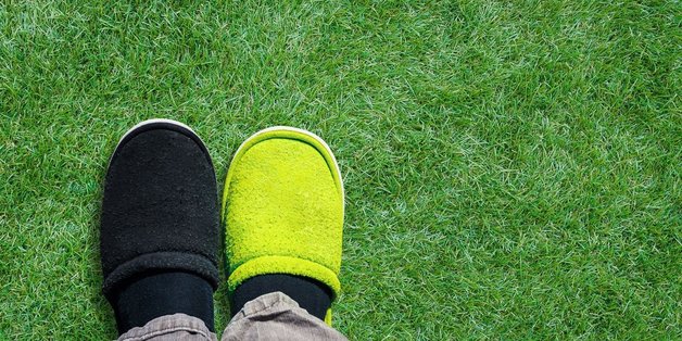 Füße mit einem grünen und einem weißen Panttoffel auf dem Rasen