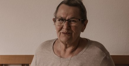Ältere Frau sitzt am Tisch bei Kaffee und Kuchen