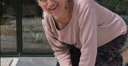 Ältere Frau legt einen Mosaikboden in einem Gewächshaus und lächelt in die Kamera