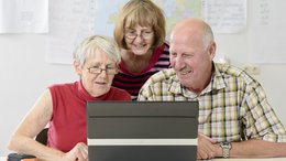 Zwei ältere Frauen und ein älterer Mann sitzen vor einem Laptop.