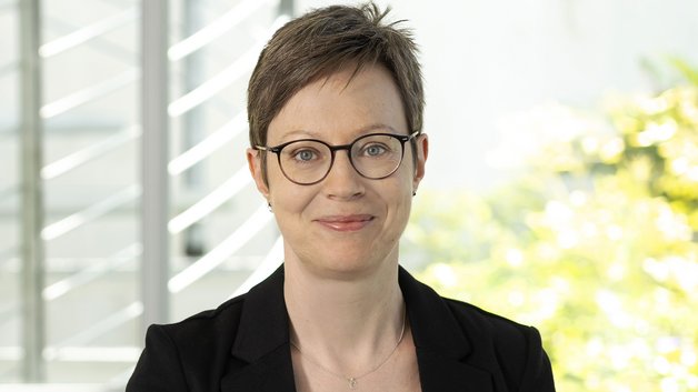 Portrait Christina Münk: Frau mittleren Alters mit kurzen braunen Haaren, Brillenträgerin. Sie trägt eine schwarzen Blazer, darunter ein grünes T-Shirt. Sie schauf lächelnd in die Kamera.