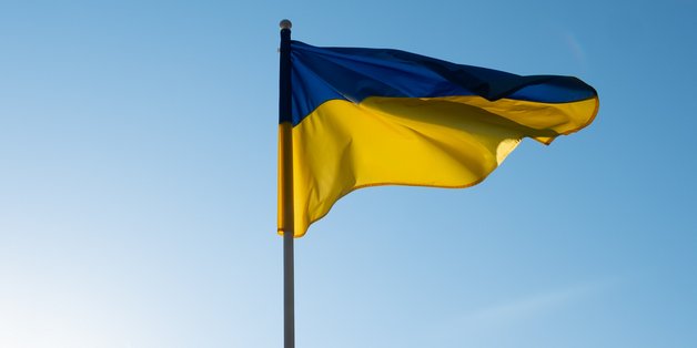 Eine Ukraine Fahne weht im Wind vor blauem Himmel.