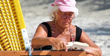 Eine Seniorin sitzt entspannt in einem Strandkorb und liest ein Buch über einen italienischen Geliebten.