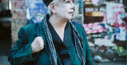 Ältere Frau mit Schiebermütze und umgehängter Gitarre