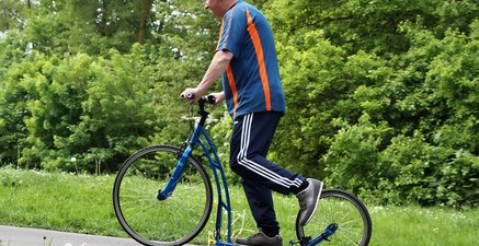 Älterer Mann in Sportkleidung fährt auf einem Tretroller.