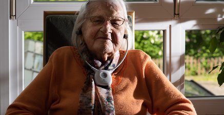 Ältere Frau sitzt in einem Sessel mit Kopfhörern, Augen geschlossen.